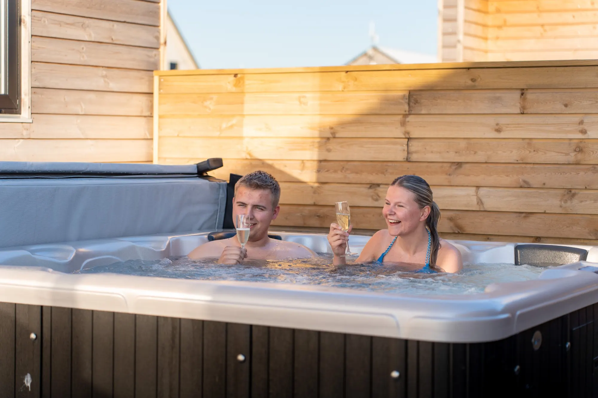 Couple raising a glass in the large private hot tub at the Premium Limfjord cabin