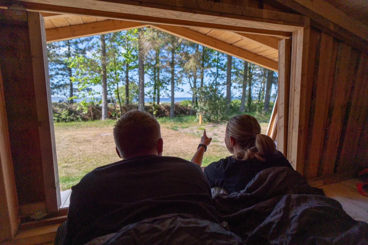 Couple lying in a shelter looking out towards the woods and the fjord